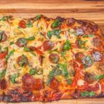 Pizza in teglia appena sfornata, con bordo dorato e soffice, su un tavolo di legno.