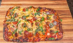 Pizza in teglia appena sfornata, con bordo dorato e soffice, su un tavolo di legno.